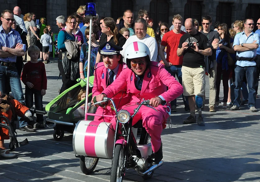 Twee verklede agenten van The Love and Peace Police op een politiebrommer met sidecar, in interactie met het publiek tijdens een straatanimatie