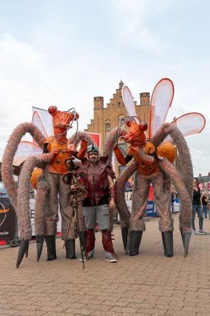 Twee steltenlopers als gigantische insecten met begeleider tijdens straatanimatie