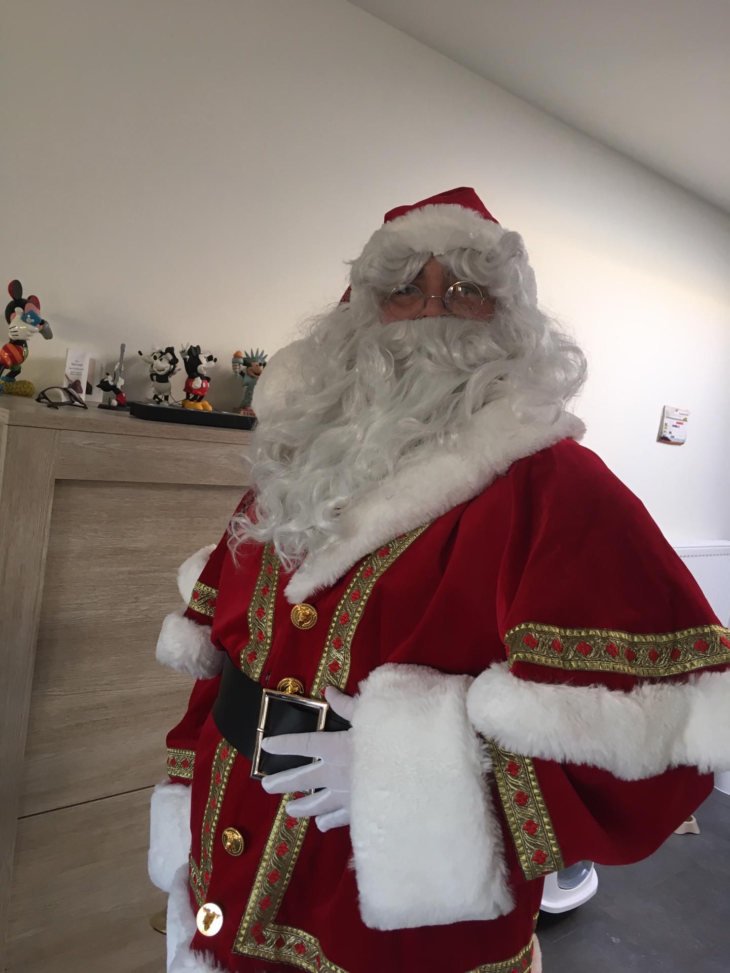 De Echte Kerstman in traditioneel rood kostuum poseert glimlachend met kinderen tijdens een kerstmarkt.