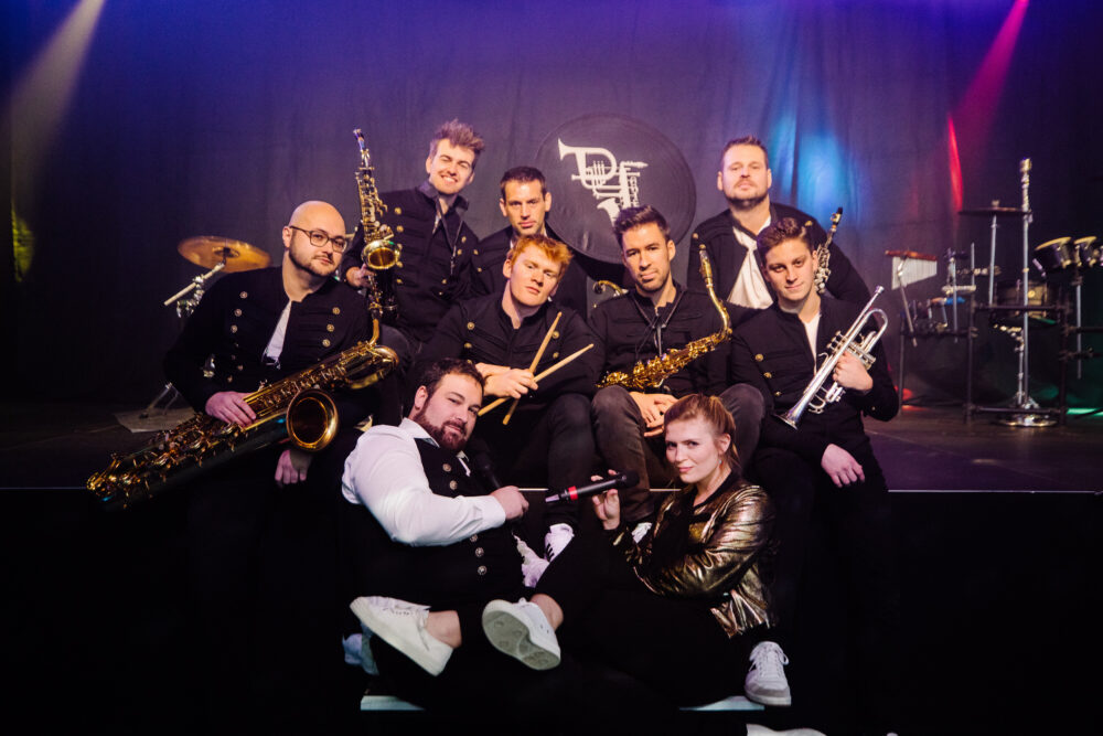 De Jartellen live op het podium met hun blazerssectie, percussionisten en zangeres in volle actie voor een uitzinnig publiek.