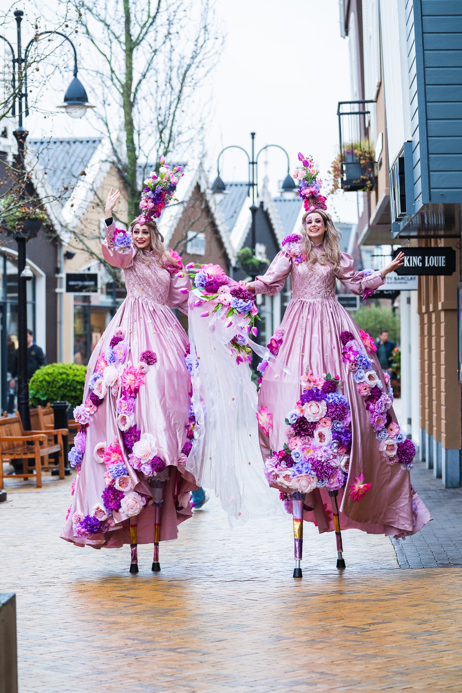 Les Fleurs steltenlopers in roze bloemenjurken met kleurrijke boeketten tijdens straatanimatie op evenement