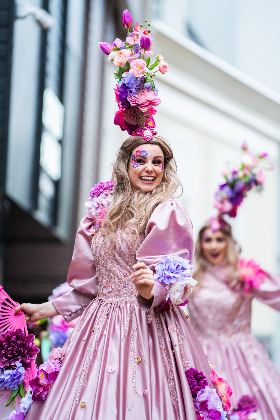 Les Fleurs steltenlopers in roze bloemenjurken met kleurrijke boeketten tijdens straatanimatie op evenement