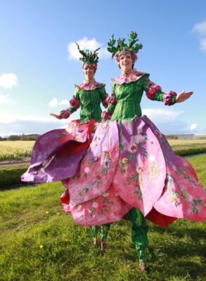 In Bloei steltenlopers met paarse bloemenkostuums en bloesemkronen tijdens lente straatanimatie op evenement